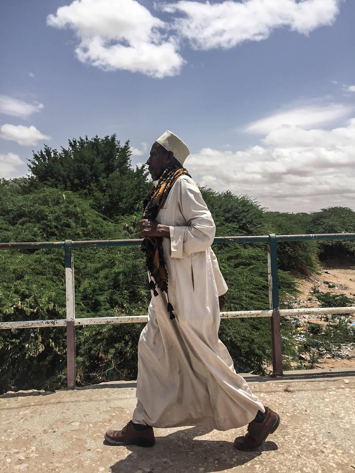A photo showing an elderly Somali man crossing a bridge